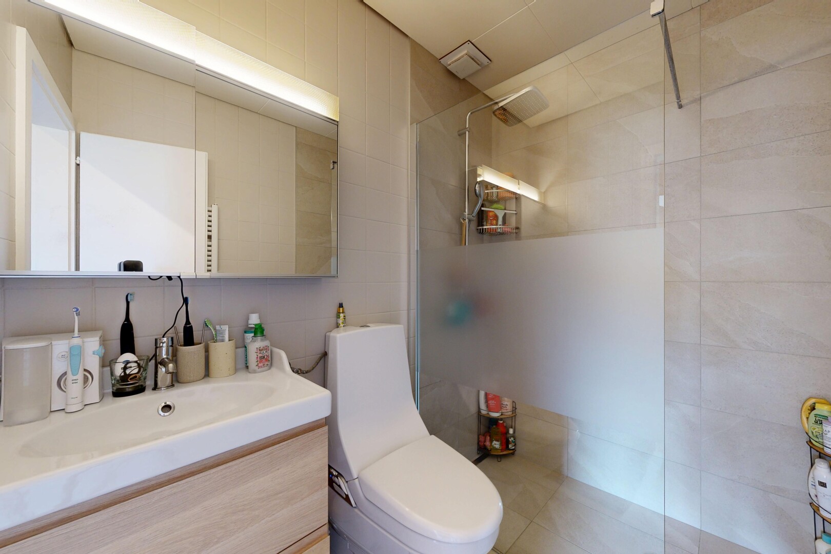 salle de bains avec douche, lavabo (ou coiffeuse selon le contexte), salle de bain complète, toilette, et mur en carrelage