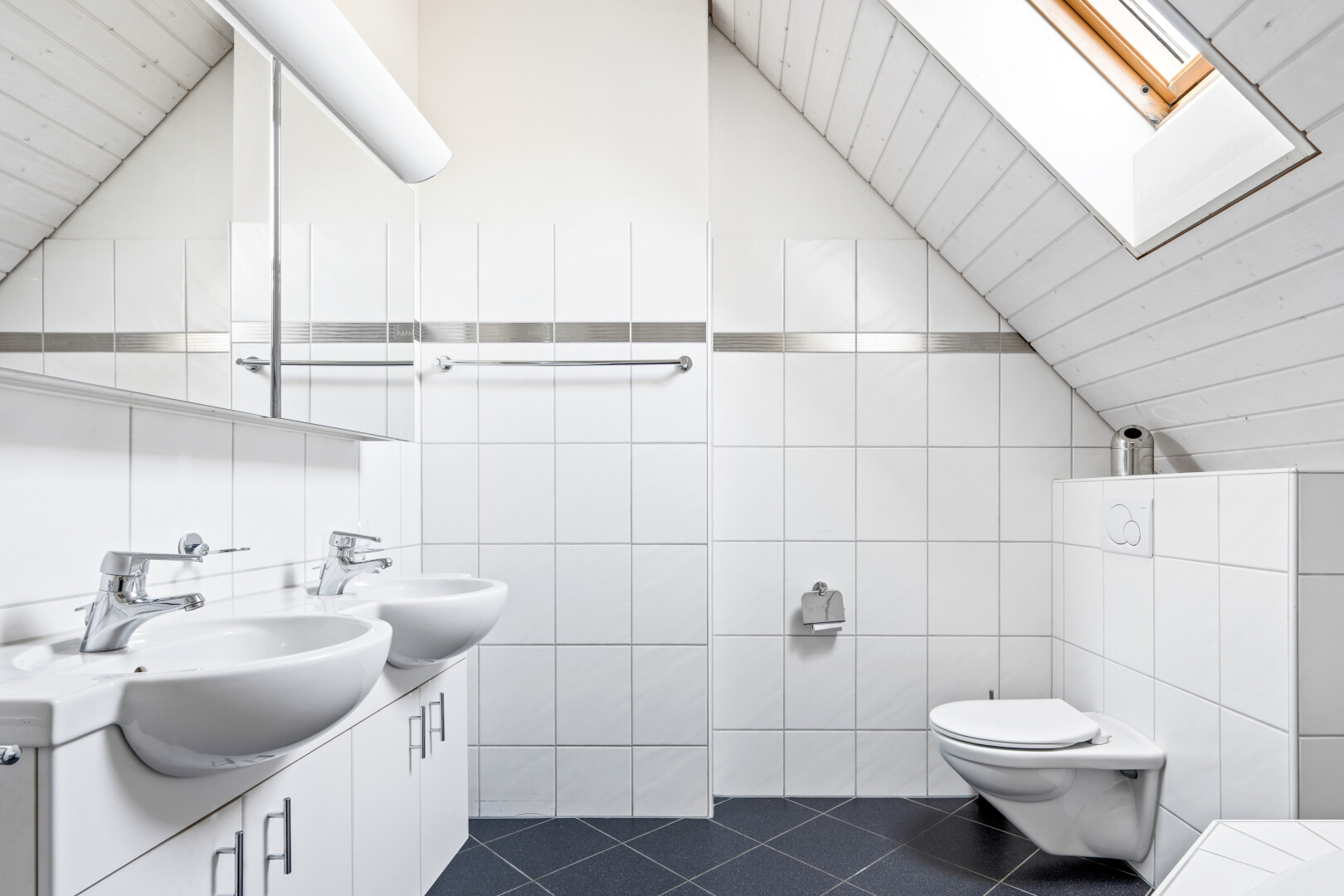 bathroom with tile walls, double vanity, dark tile patterned floors, vaulted ceiling, and a skylight