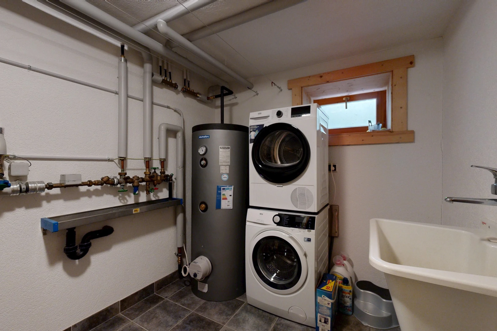 buanderie avec évier, lave-linge et sèche-linge superposés, chauffe-eau, sous-sol, et inside property