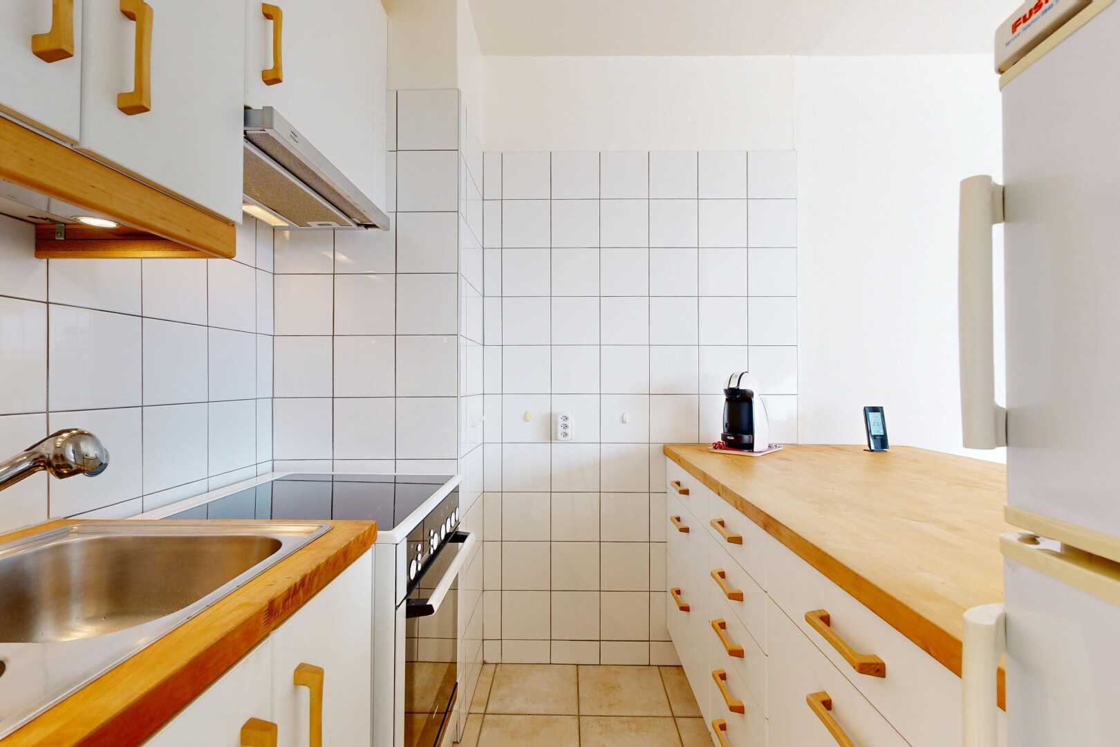 cuisine avec armoires blanches, réfrigérateur, cuisinière, hotte, et sol en carrelage