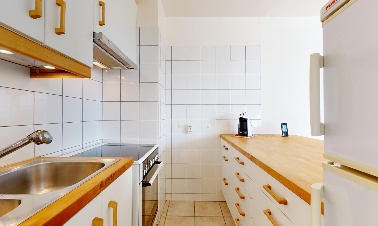 cuisine avec armoires blanches, réfrigérateur, cuisinière, hotte, et sol en carrelage