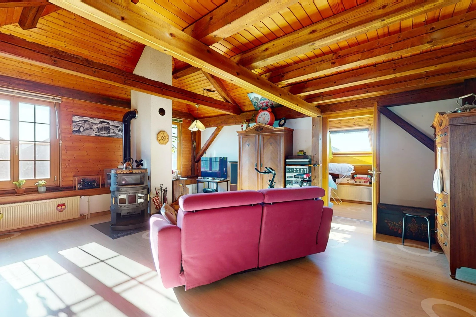 salon avec radiateur, poutres apparentes, plafond de bois, lumière naturelle, et poêle à bois