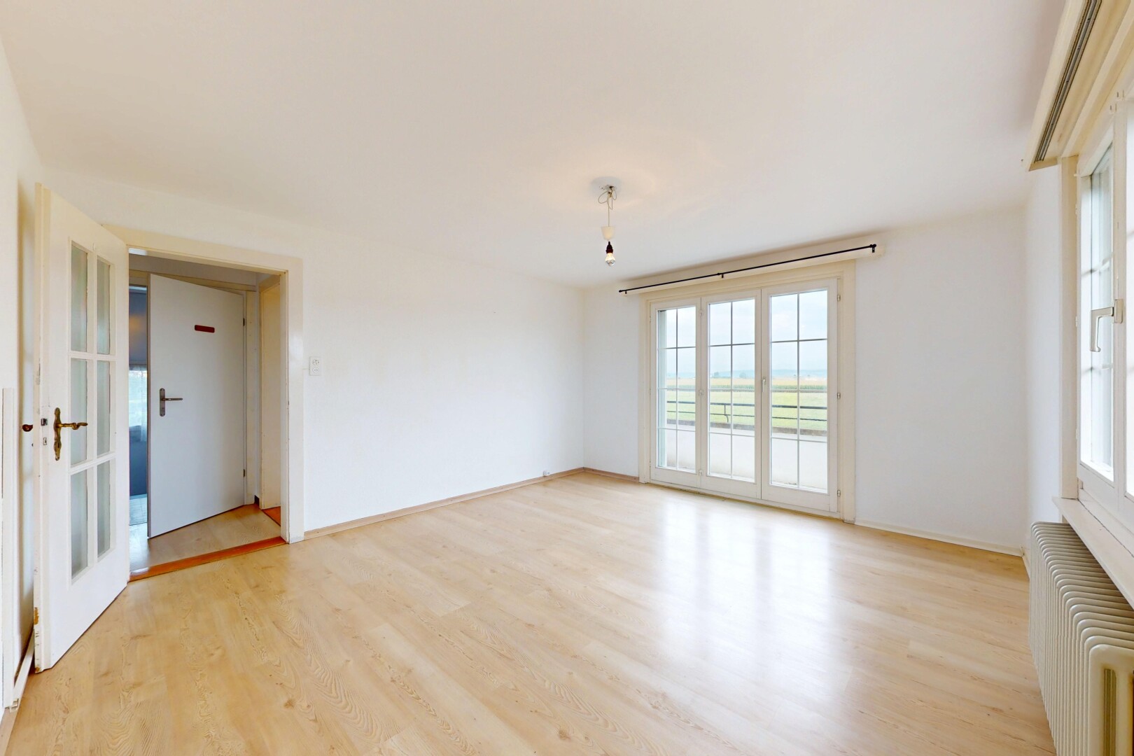 pièce vide avec radiateur, lumière naturelle, natural light, portes-fenêtres, et sol en finition bois
