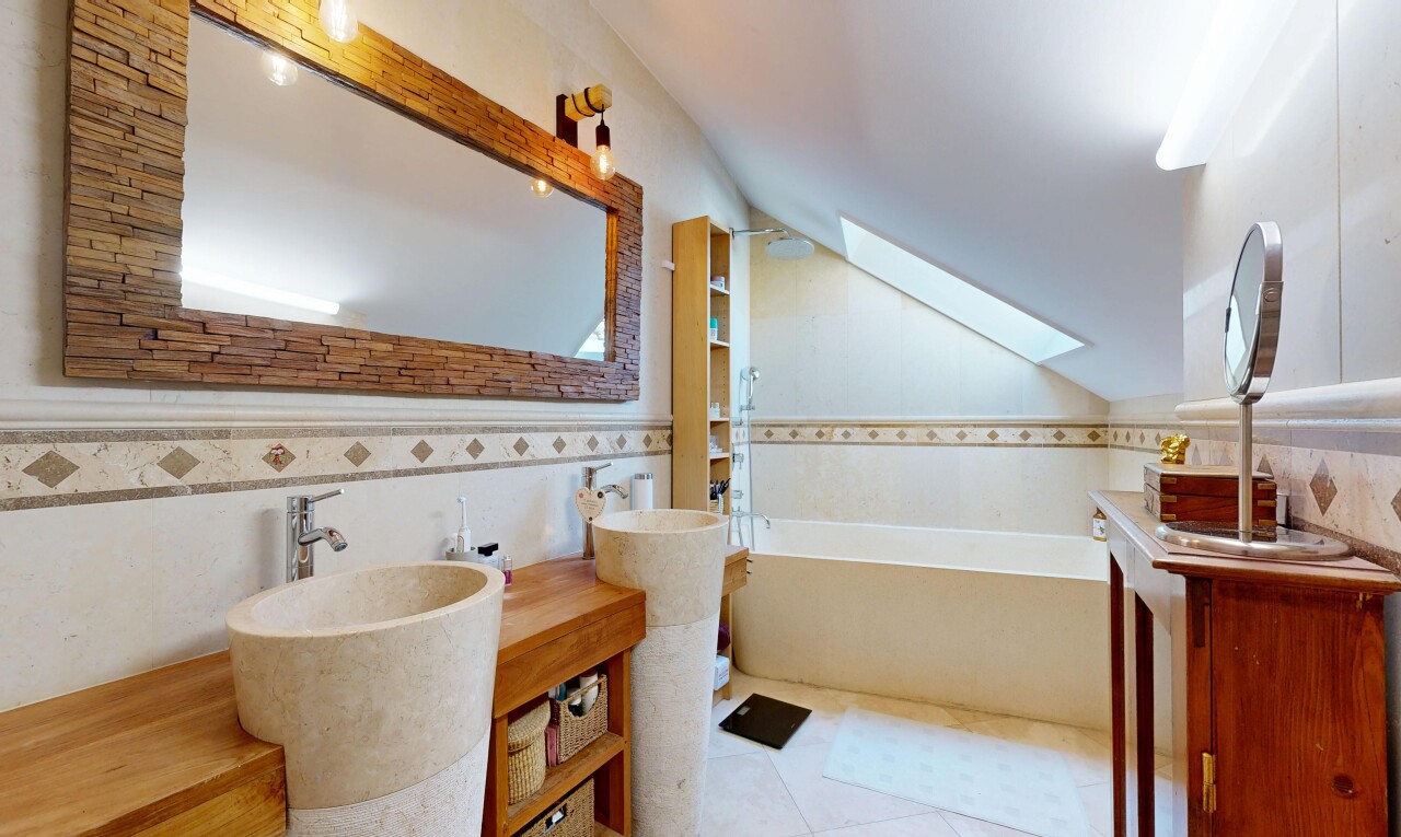 full bathroom featuring tile walls, a bath, double vanity, vaulted ceiling with skylight, and a sink