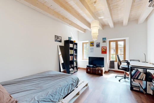 chambre avec portes-fenêtres, télévision, plafond à poutres, et lumière naturelle