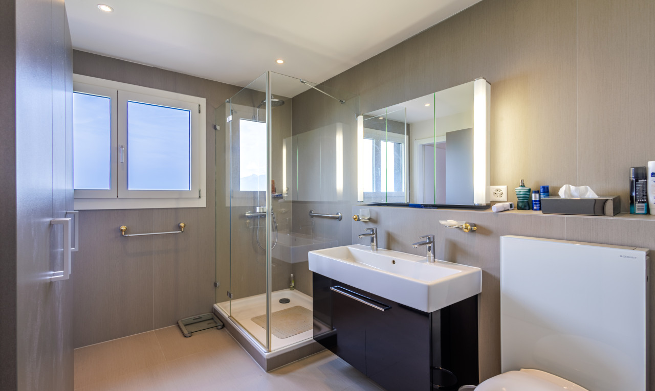 badezimmer mit einer fülle von natürlichen licht, waschtisch mit umfangreichem schrankraum, dusche mit duschenentür und spiegel