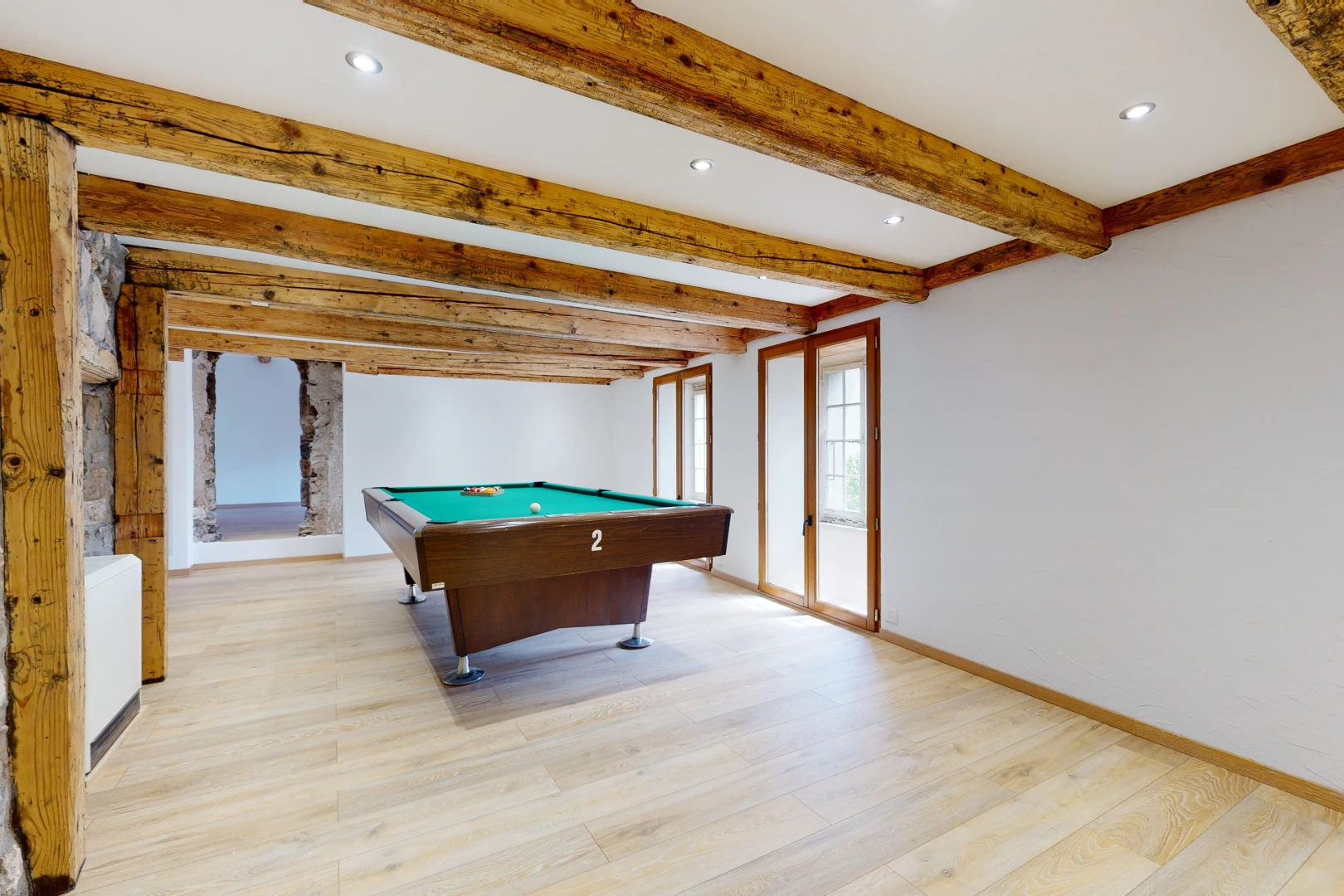 salle de jeux avec poutres apparentes, lumière naturelle, et parquet