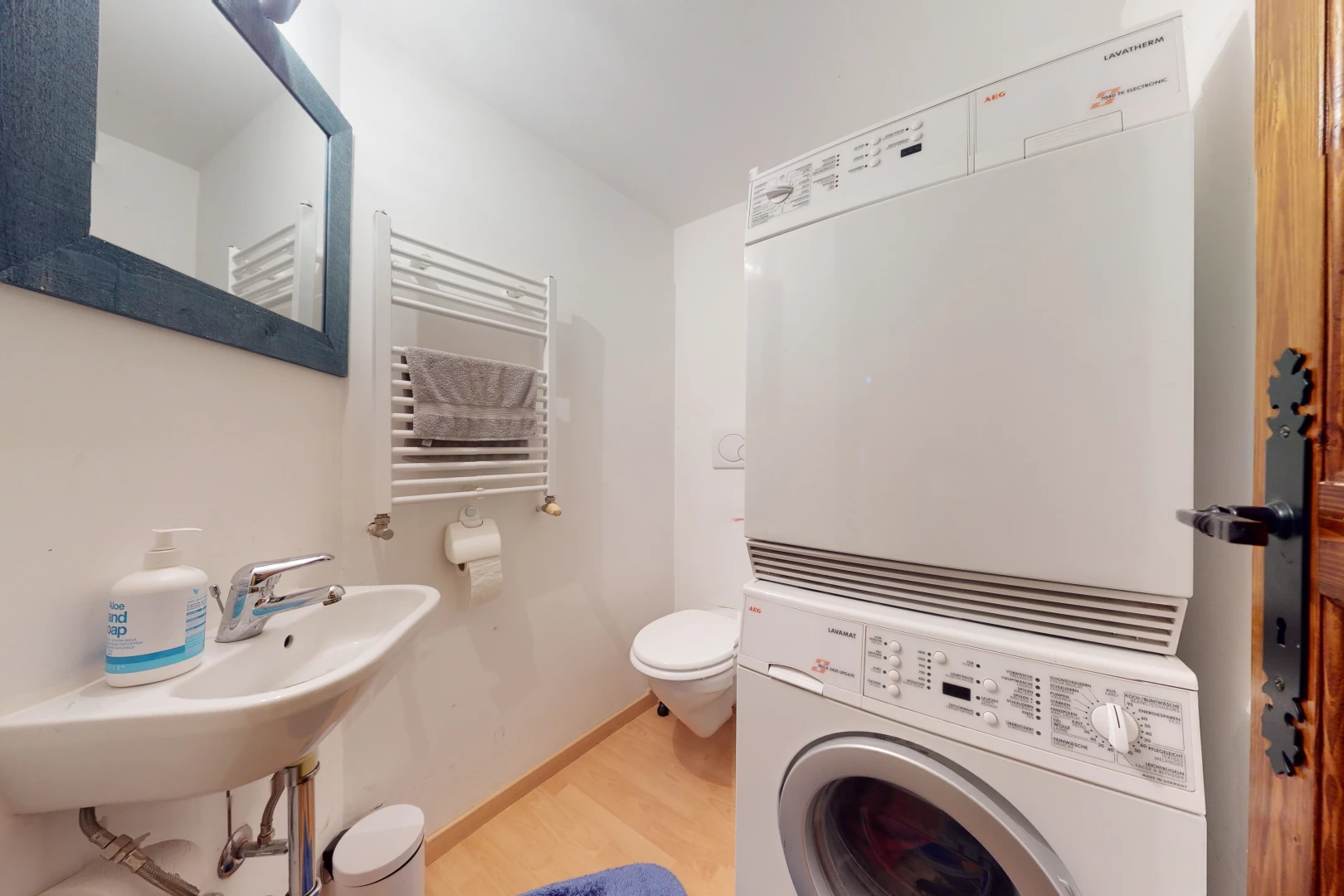 salle de bains avec parquet, radiateur, machine à laver / sèche-linge, toilette, miroir, et vasque
