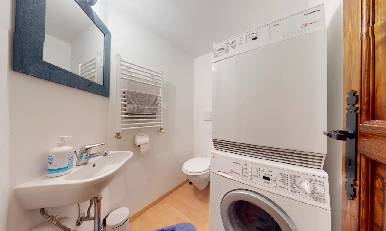 salle de bains avec parquet, radiateur, machine à laver / sèche-linge, toilette, miroir, et vasque