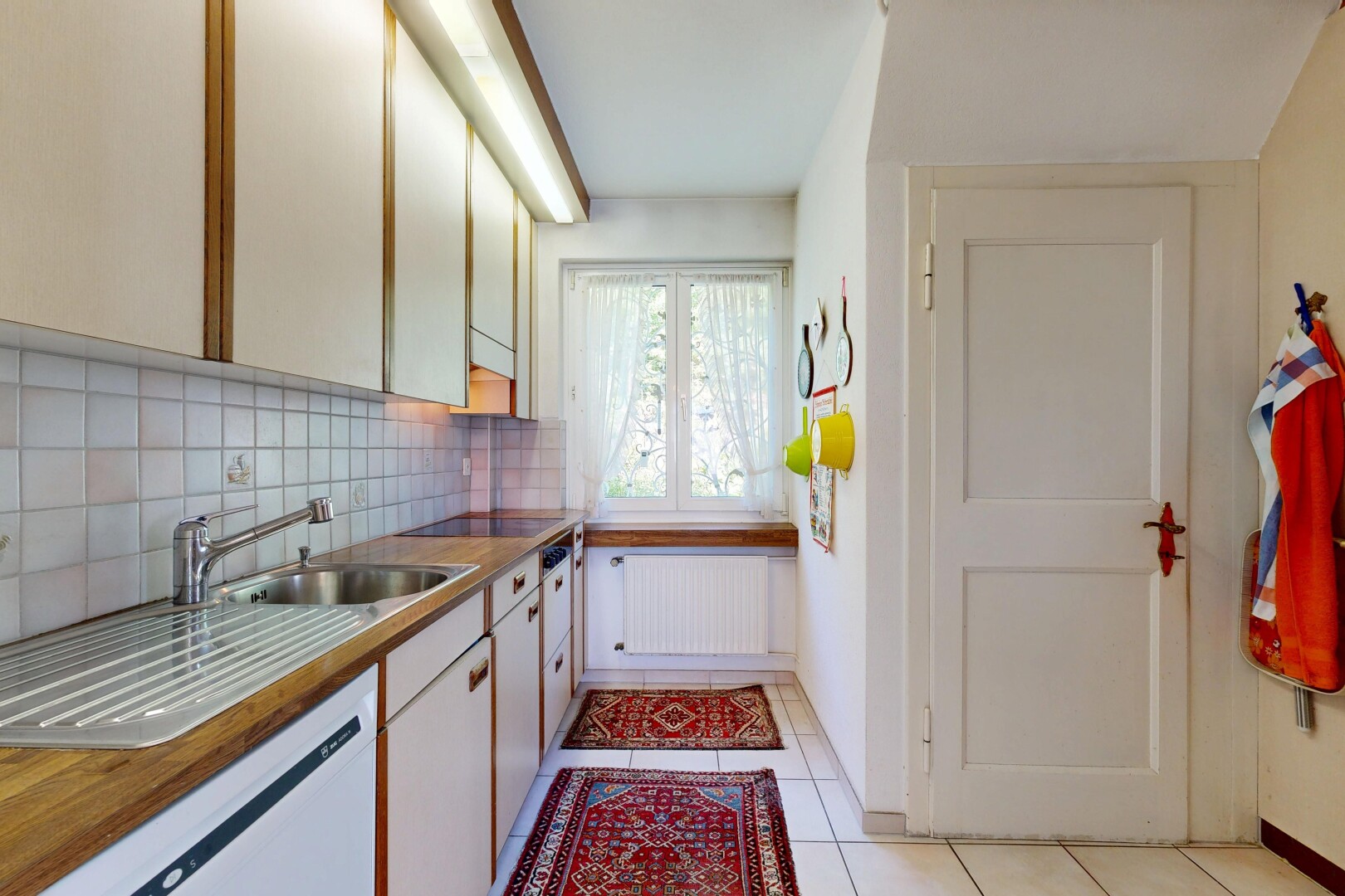 two tone kitchen featuring backsplash, light tile patterned floors, radiator heating unit, dishwasher, and black electric stovetop
