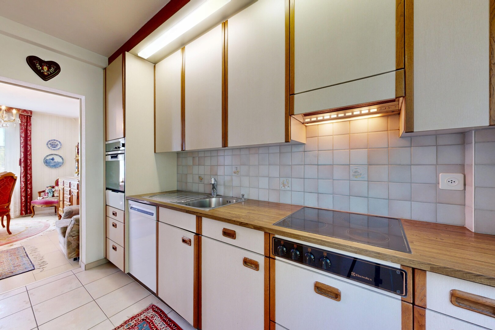 two tone kitchen with tasteful backsplash, light tile patterned floors, black electric cooktop, dishwasher, and two tone cabinetry