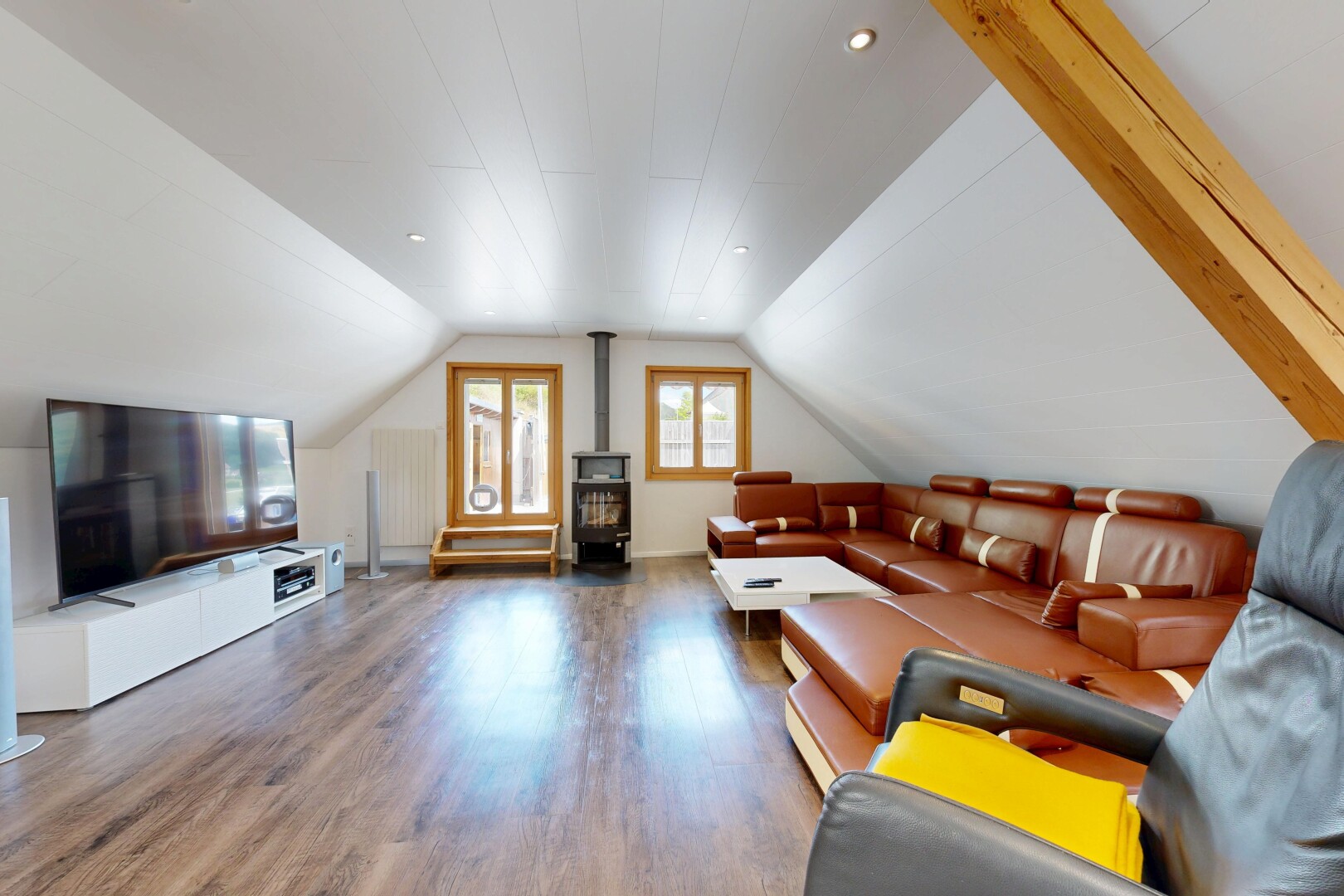 salon avec pièce supplémentaire, sol en finition bois, wood finish floor, télévision, et poêle à bois