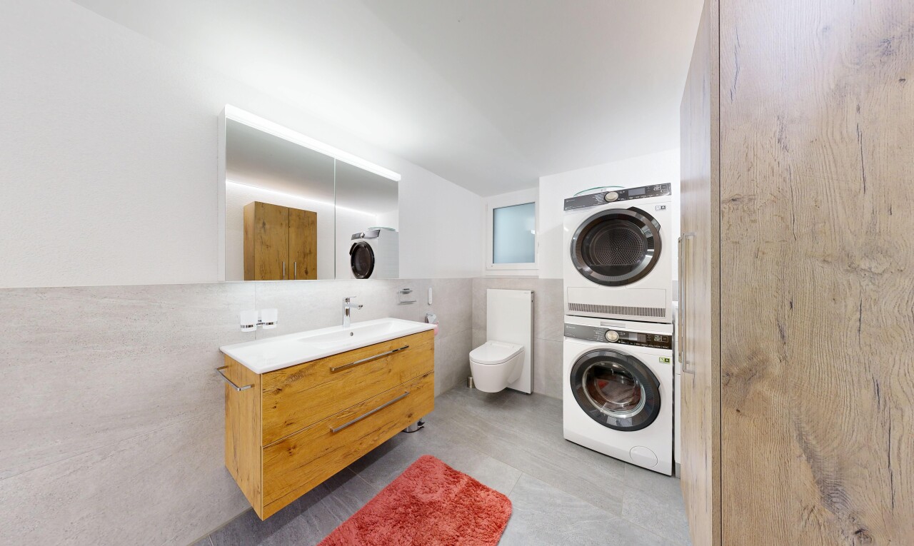 salle de bains avec mur en carrelage, tile wall, lavabo (ou coiffeuse selon le contexte), lave-linge et sèche-linge superposés, et miroir