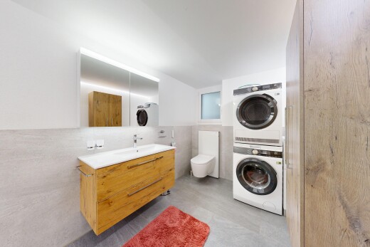 salle de bains avec mur en carrelage, tile wall, lavabo (ou coiffeuse selon le contexte), lave-linge et sèche-linge superposés, et miroir