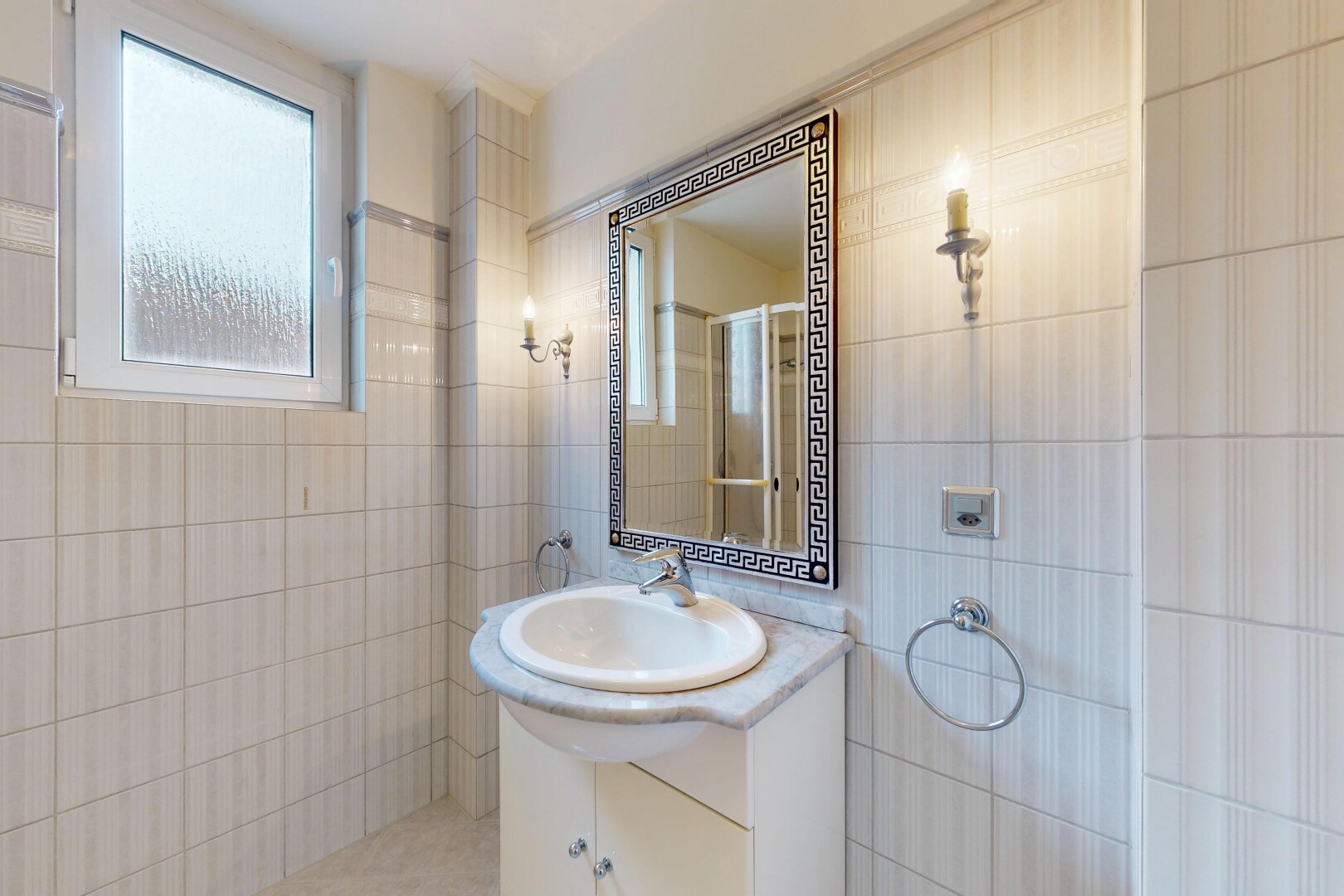 salle de bains avec mur en carrelage, tile wall, lavabo (ou coiffeuse selon le contexte), miroir, et lumière naturelle