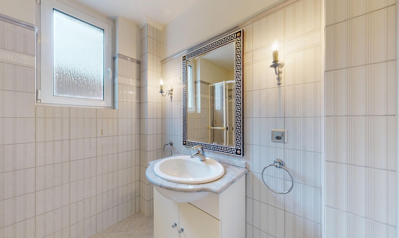 salle de bains avec mur en carrelage, tile wall, lavabo (ou coiffeuse selon le contexte), miroir, et lumière naturelle
