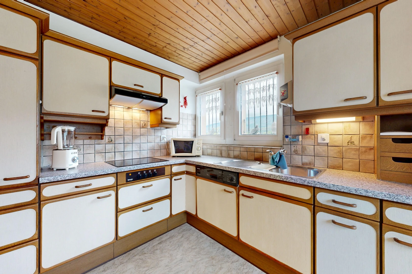 dual tone kitchen with light countertops, wooden ceiling, two tone color scheme, decorative backsplash, and white appliances