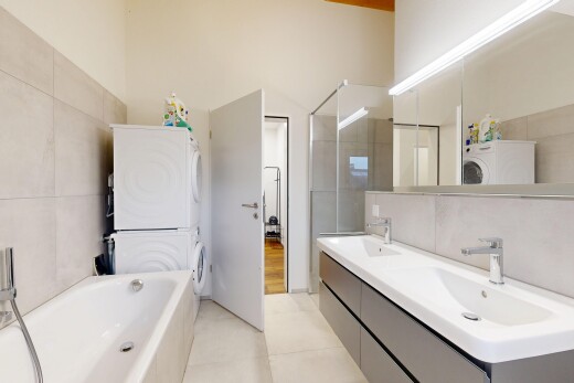 full bathroom with tile walls, double vanity, stacked washing machine and dryer, a garden tub, and a walk in shower