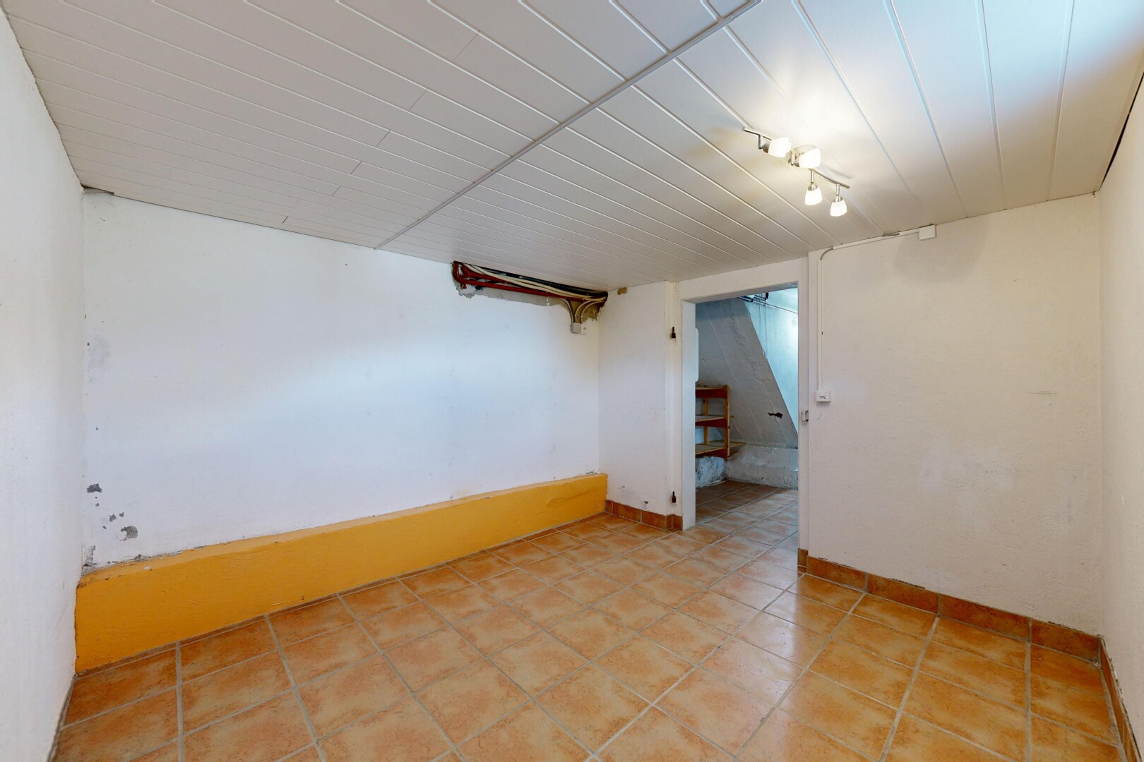 pièce vide avec éclairage sur rail, drywall, cloison sèche, sous-sol, et escaliers