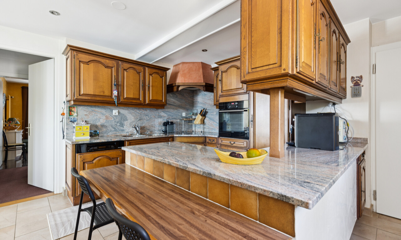 kitchen with a breakfast bar area, tasteful backsplash, wood finish cabinetry, light stone counters, and beamed ceiling