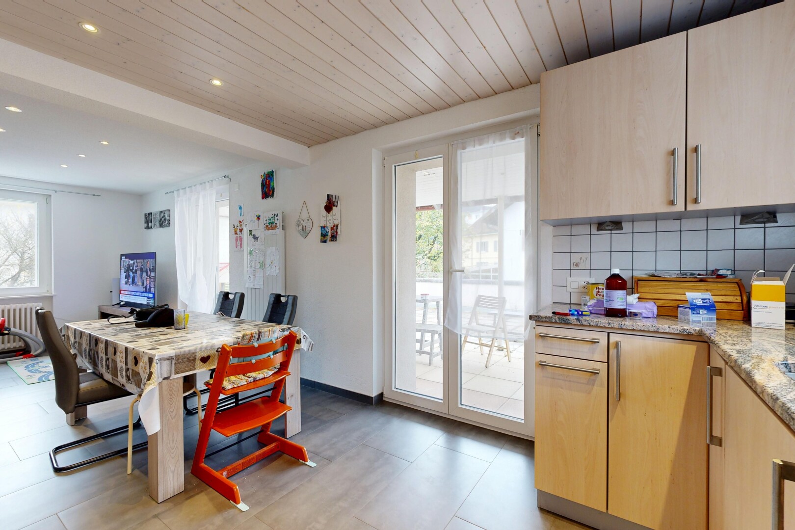 cuisine avec armoires marron clair, plafond en bois, wood ceiling, plans de travail en pierre, et lumière naturelle