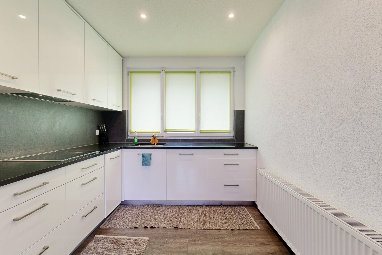 cuisine avec armoires blanches, radiateur, plans de travail, wood finish floor, et inside property