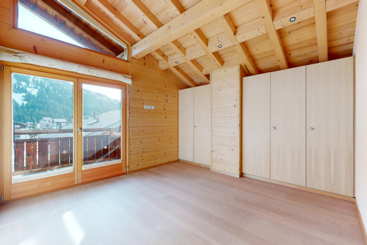 pièce vide avec mur en bois, plancher de bois, lumière naturelle, plafond voûté, et poutres apparentes