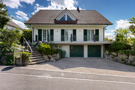 view of home featuring a balcony, stucco siding, an attached garage, a chimney, and decorative driveway