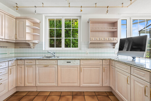 kitchen with open shelves, light wood finish cabinetry, light stone counters, and paneled dishwasher