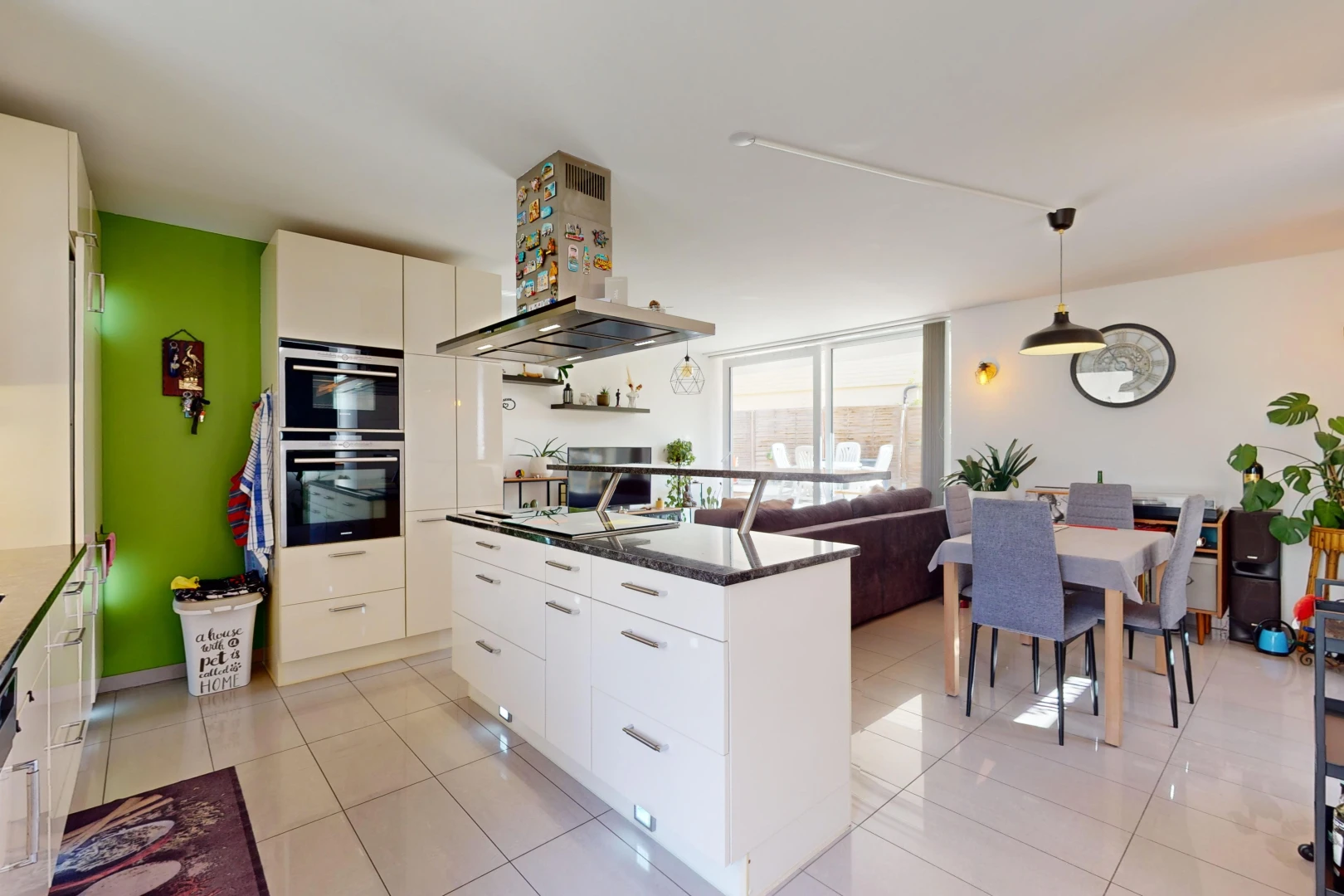 kitchen with stainless steel double oven, light tile patterned flooring, hanging light fixtures, and wall chimney range hood