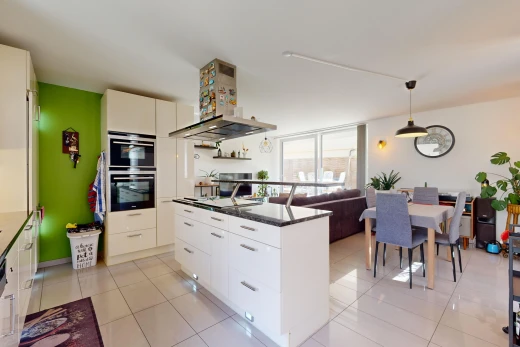 kitchen with stainless steel double oven, light tile patterned flooring, hanging light fixtures, and wall chimney range hood