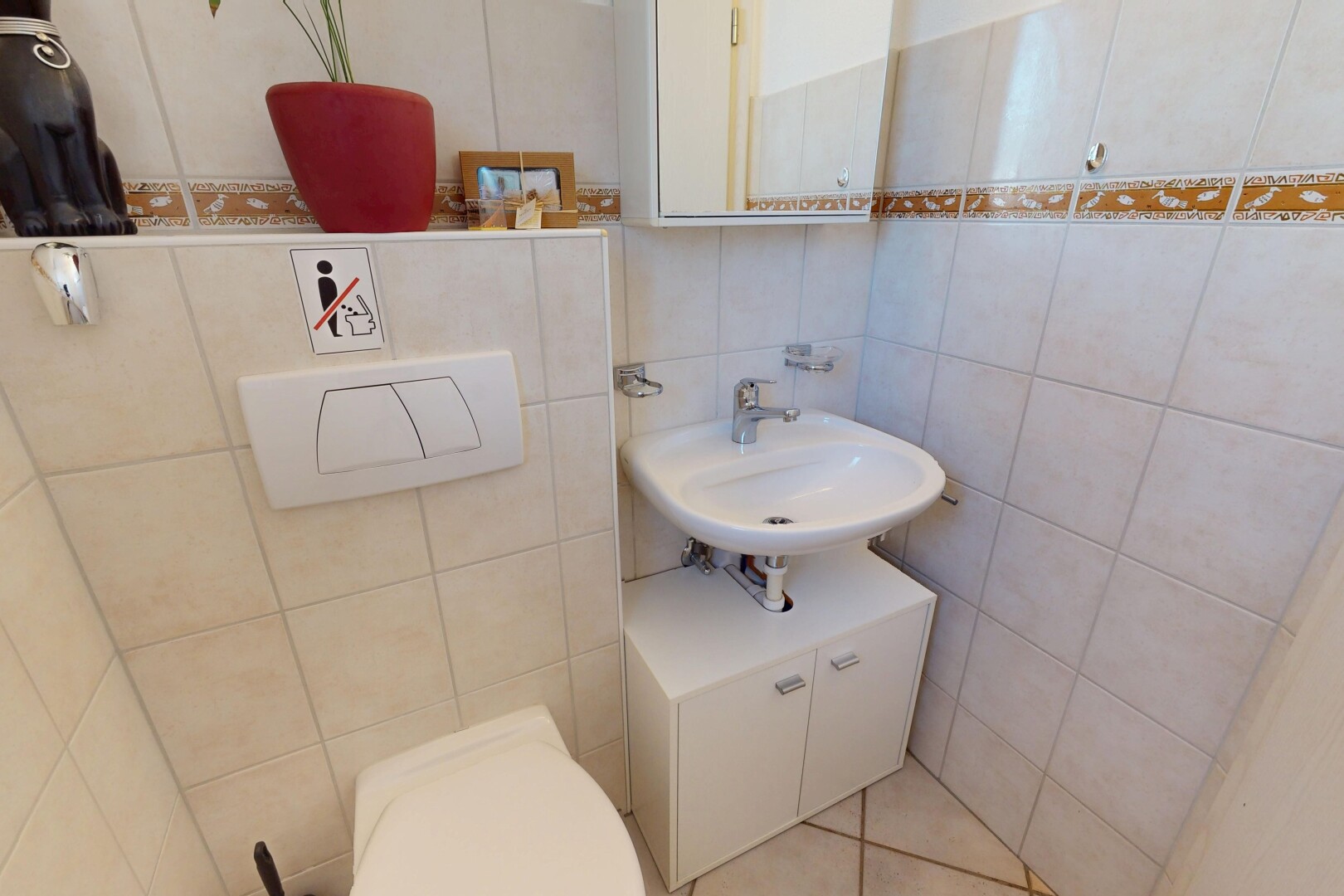 salle de bains avec miroir, mur en carrelage, toilette, et évier