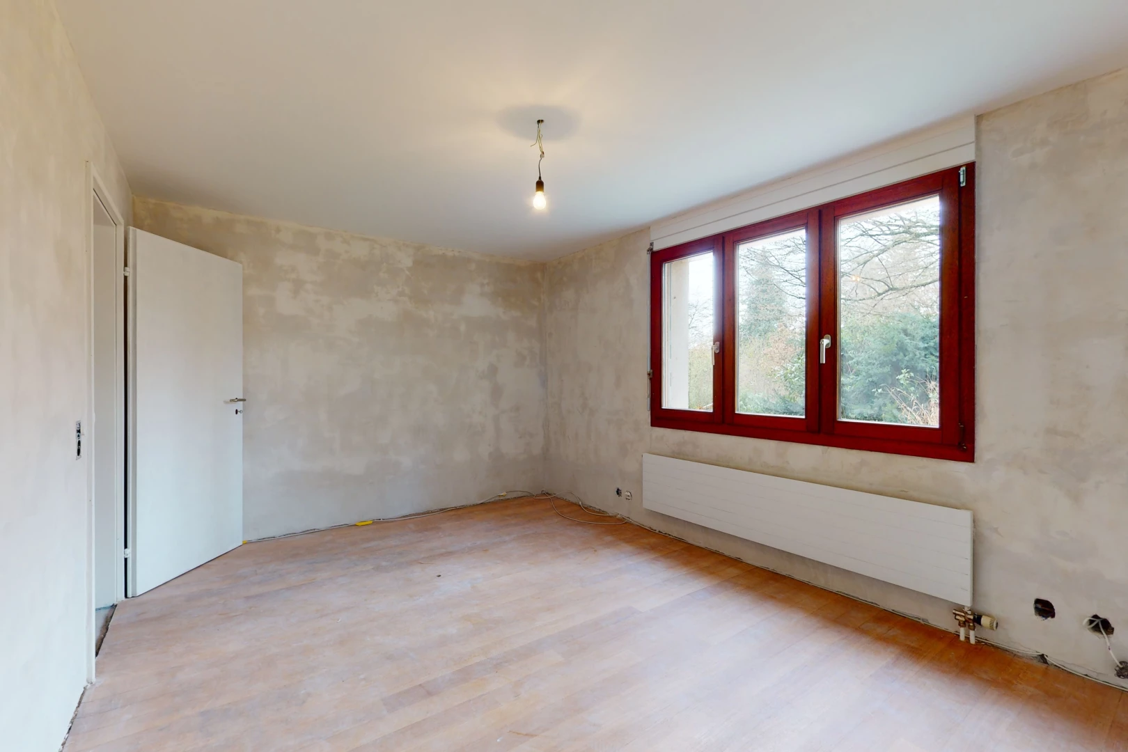 chambre vide avec lumière naturelle, parquet, et radiateur
