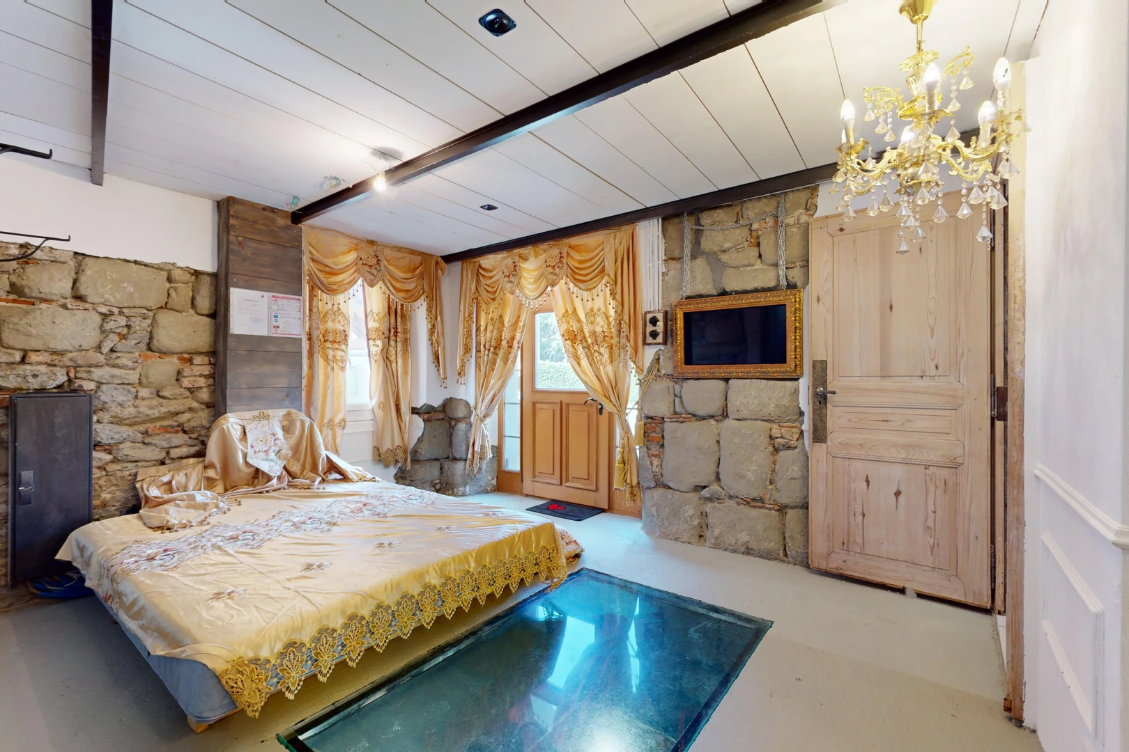 chambre avec sol en béton, lumière naturelle, mur en pierre, et poutres apparentes