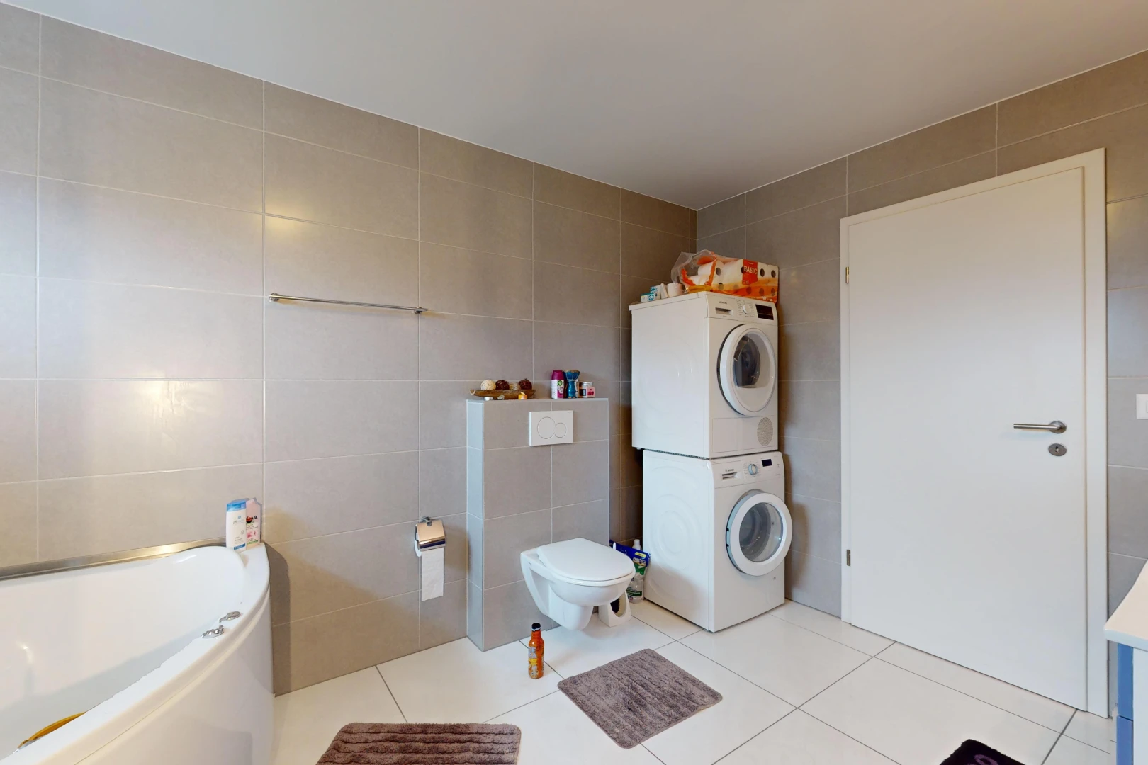 salle de bains avec baignoire, toilettes, carrelage, machine à laver / sèche-linge superposés, et mur carrelé