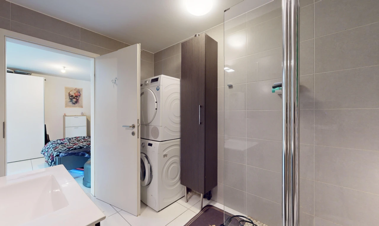 salle de bains avec machine à laver / sèche-linge superposés, douche, et carrelage