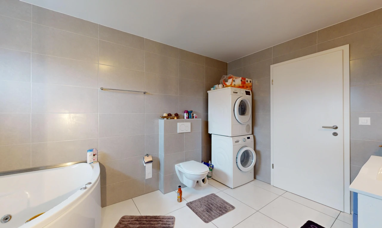 salle de bains avec baignoire, toilettes, carrelage, machine à laver / sèche-linge superposés, et mur carrelé