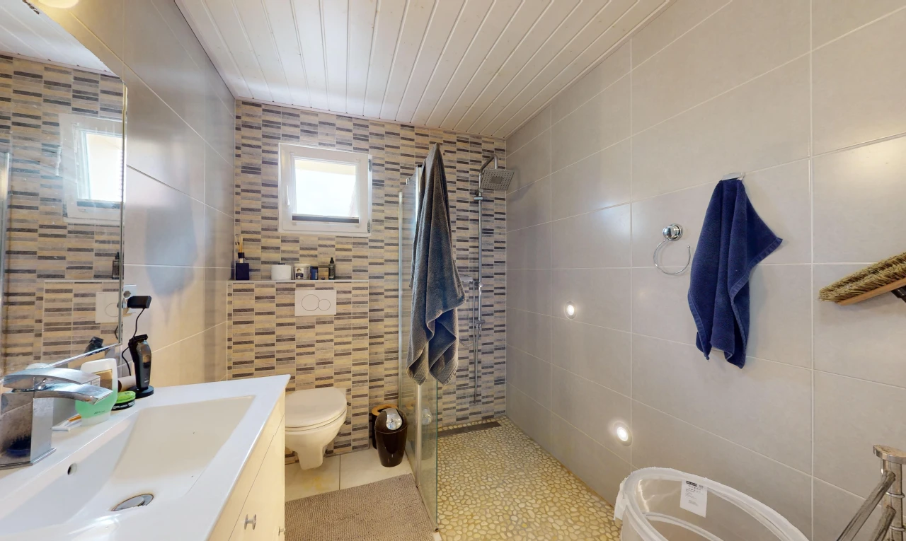 salle de bains avec douche, mur carrelé, toilettes, meuble-lavabo, et lumière naturelle