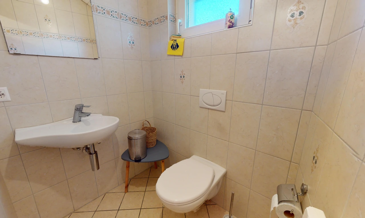 salle de bains avec mur carrelé, toilettes, lumière naturelle, et carrelage