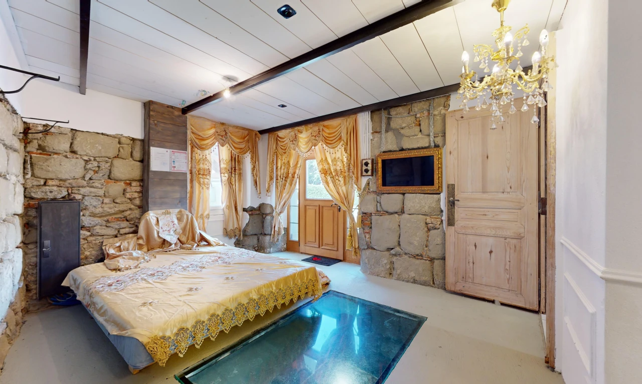 chambre avec sol en béton, lumière naturelle, mur en pierre, et poutres apparentes