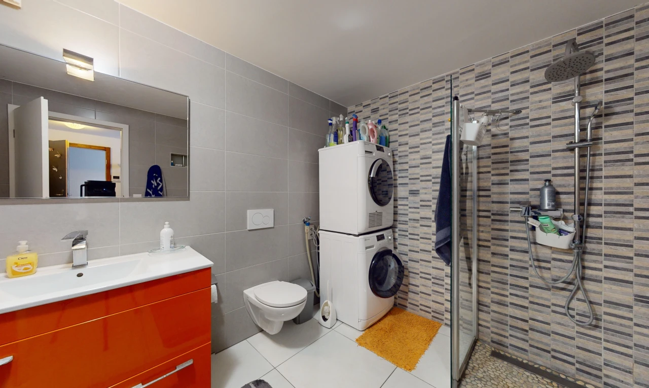 salle de bains avec miroir, douche, mur carrelé, meuble-lavabo, et machine à laver / sèche-linge superposés