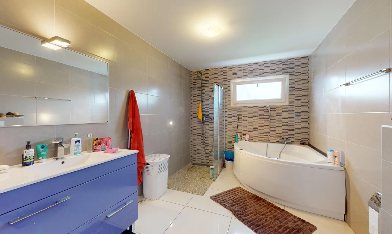 salle de bains avec douche, mur carrelé, meuble-lavabo, lumière naturelle, et miroir