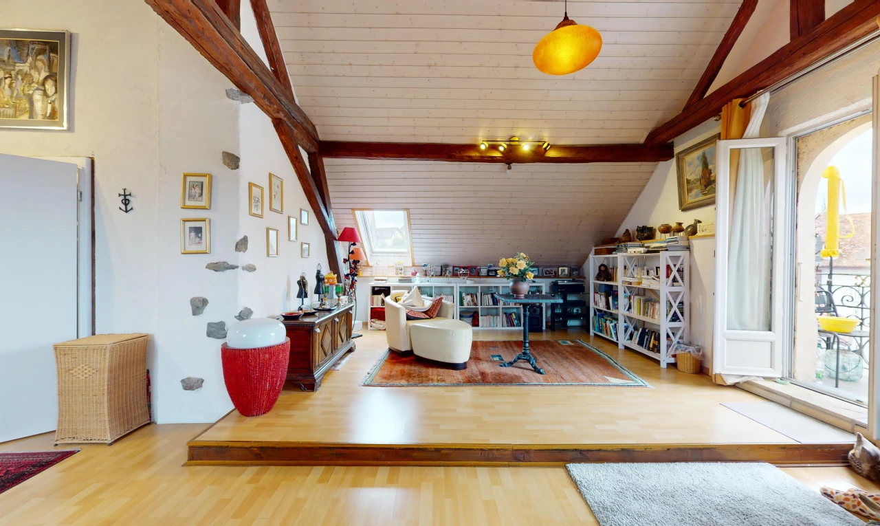 salon avec lumière naturelle, poutres apparentes, plancher de bois, et plafond voûté
