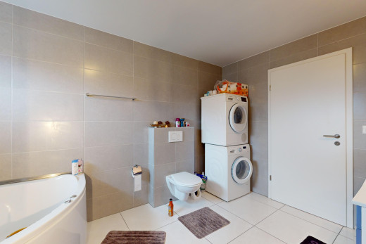 salle de bains avec baignoire, toilettes, carrelage, machine à laver / sèche-linge superposés, et mur carrelé