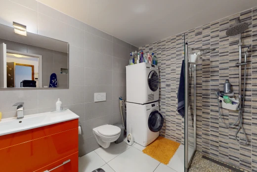 bathroom with tile walls, stacked washer and dryer, a shower with shower door, vanity, and toilet