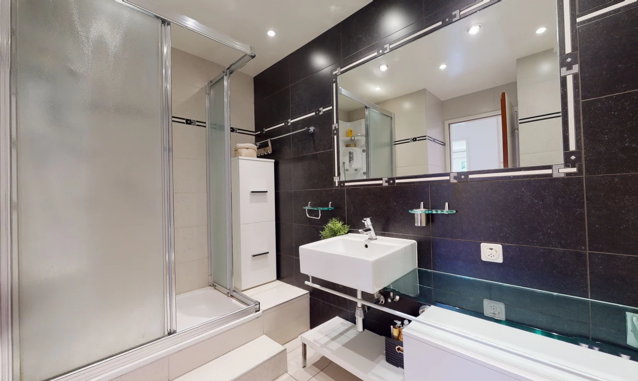salle de bains avec miroir, porte de douche, combiné baignoire-douche, et vasque