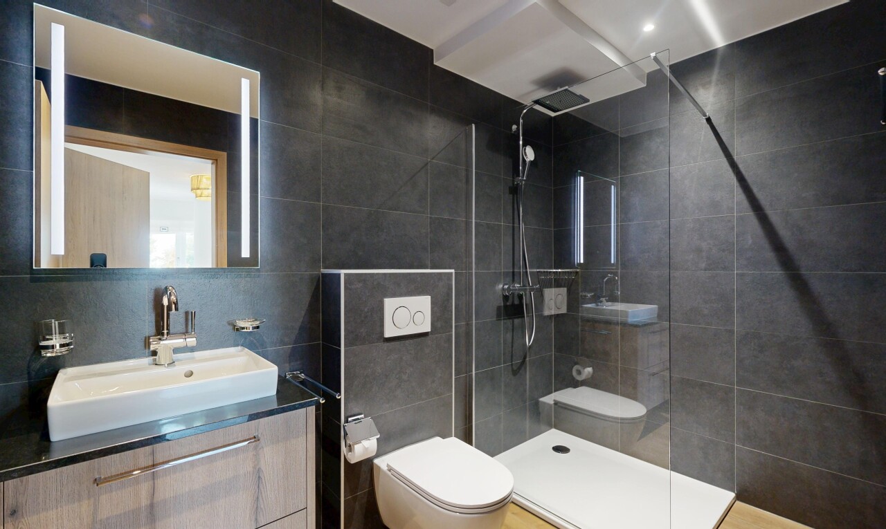 salle de bains avec mur en carrelage, tile wall, miroir, lavabo (ou coiffeuse selon le contexte), et toilette