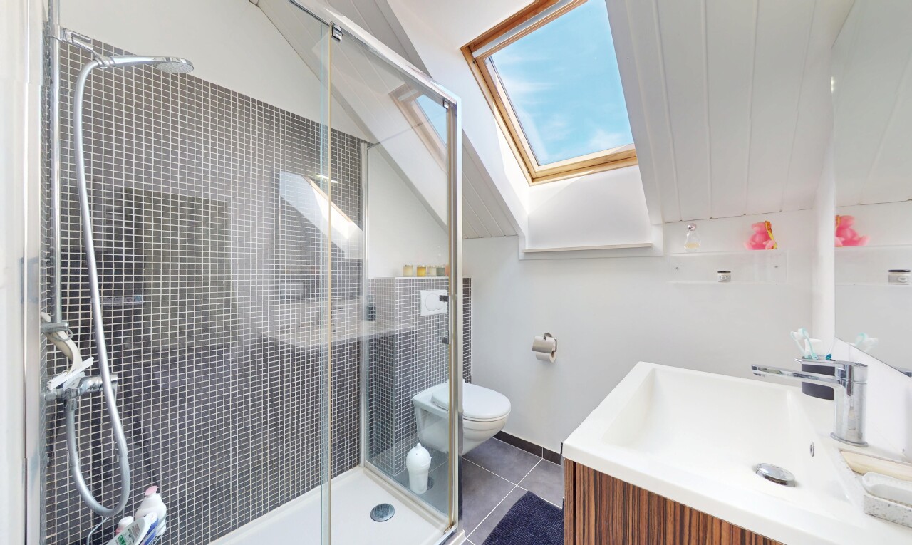 salle de bains avec puits de lumière, lavabo (ou coiffeuse selon le contexte), douche, toilette, et sol en carrelage