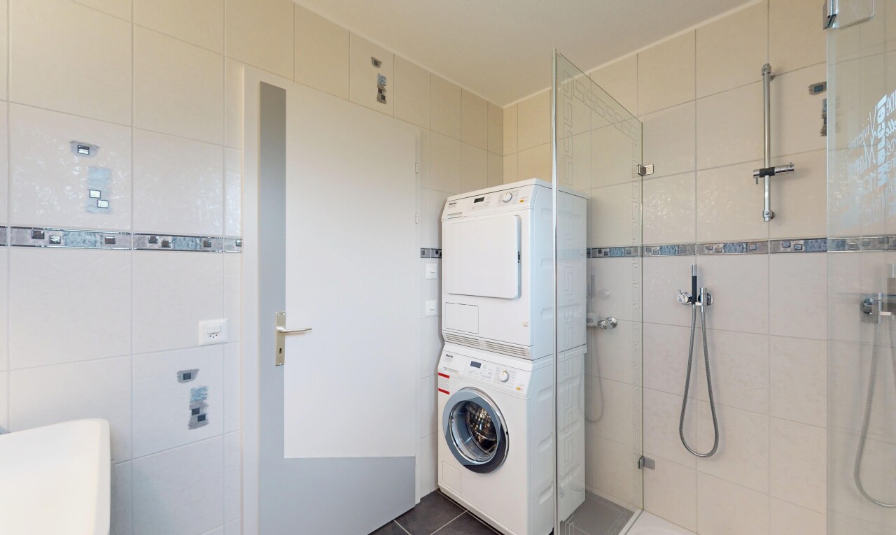 buanderie avec tile wall, mur en carrelage, lave-linge et sèche-linge superposés, tile floor, et sol en carrelage