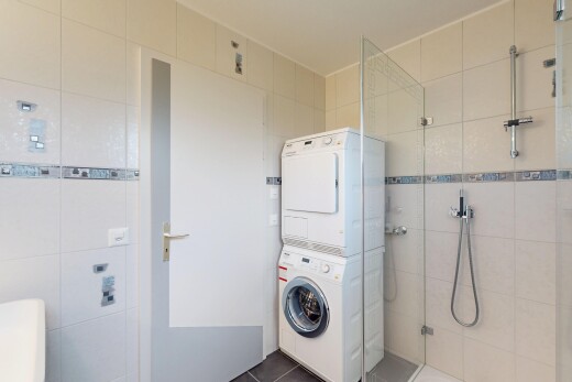 buanderie avec tile wall, mur en carrelage, lave-linge et sèche-linge superposés, tile floor, et sol en carrelage